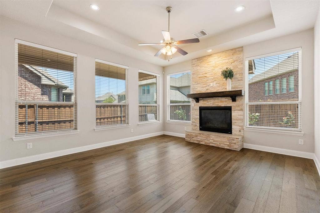 4109 Rainey Street, McKinney, TX 75070 Stone-clad fireplace with a dark wood-finish mantel, wood-finish flooring, and a ceiling fan