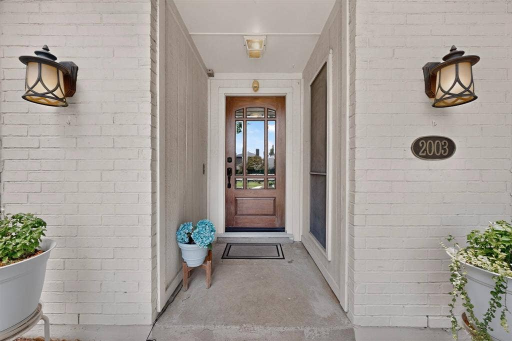 2003 J J Pearce Drive, Richardson, TX 75081 Welcoming entry featuring a wood-finish door with decorative glass, two wall-mounted lanterns, a concrete entry porch, and a white brick exterior