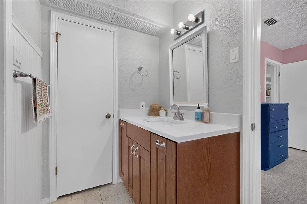 2003 J J Pearce Drive, Richardson, TX 75081 Bathroom vanity featuring a single basin sink, white countertop, wood-finish cabinetry, and chrome hardware