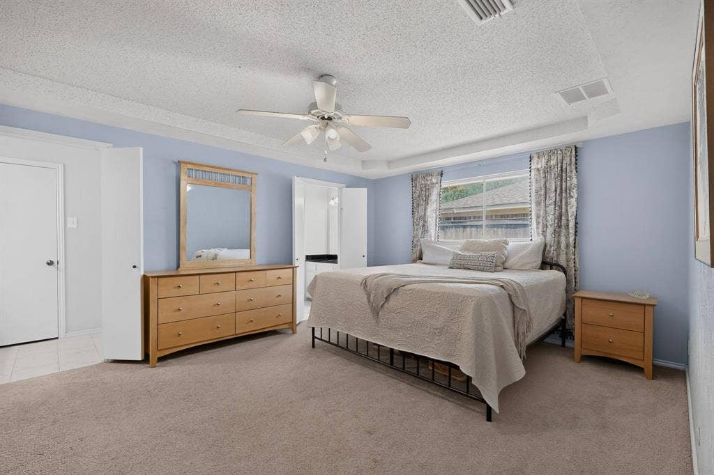 2003 J J Pearce Drive, Richardson, TX 75081 Carpeted bedroom featuring a tray ceiling, ceiling fan, and a window with a white privacy fence visible beyond