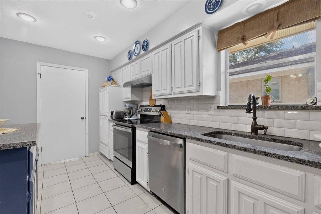 2003 J J Pearce Drive, Richardson, TX 75081 Contemporary kitchen featuring white cabinetry, subway tile backsplash, dark speckled countertops, stainless steel appliances, and tile flooring