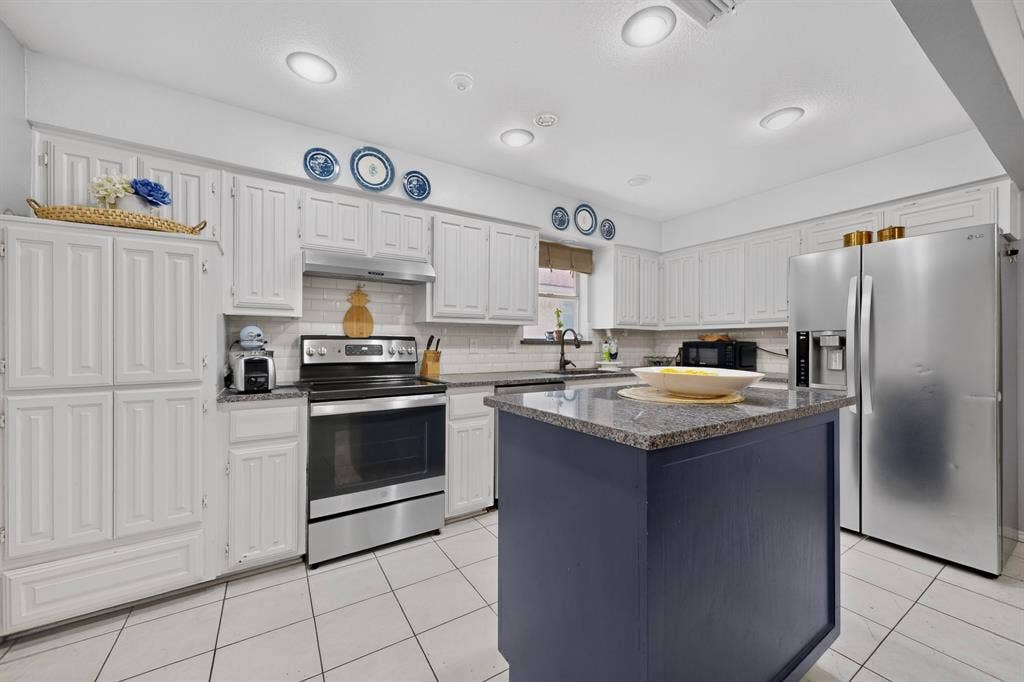 2003 J J Pearce Drive, Richardson, TX 75081 Kitchen featuring a movable central island with a stone countertop, white cabinetry, subway tile backsplash, stainless steel appliances, and recessed lighting