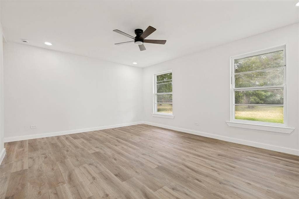 Spacious interior featuring wood-finish flooring, two large windows, a ceiling fan, recessed lighting, and white baseboards