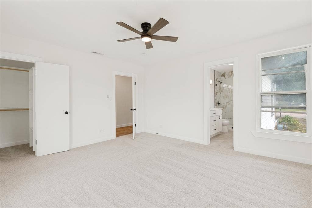 Carpeted room featuring a ceiling fan with light, an open closet with shelving, a window providing natural light, and an adjacent bathroom with a vanity and tiled shower