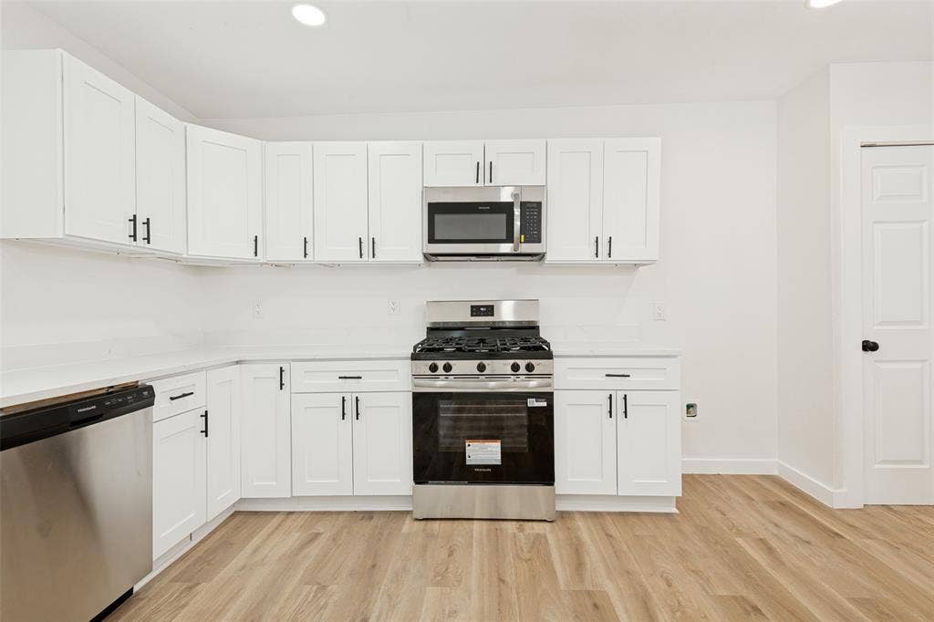 Modern kitchen featuring white shaker cabinetry, stainless steel appliances, light-toned countertops, wood-finish flooring, and recessed lighting