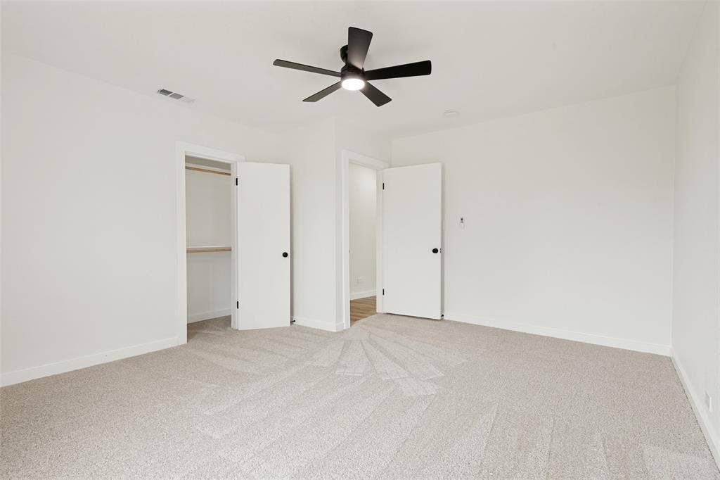 Neutral-toned carpeted room featuring a ceiling fan with black blades, white walls, and white trim