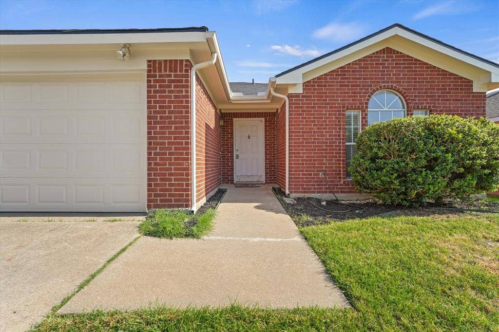 2312 Corral Drive, Fort Worth, TX 76133 Welcoming brick front elevation featuring a two-car garage, arched window detail, and concrete driveway leading to the entrance