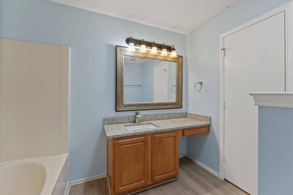 2312 Corral Drive, Fort Worth, TX 76133 Spa-inspired primary bathroom featuring a wood-finish vanity with dual sinks, granite countertop, and framed mirror with integrated lighting