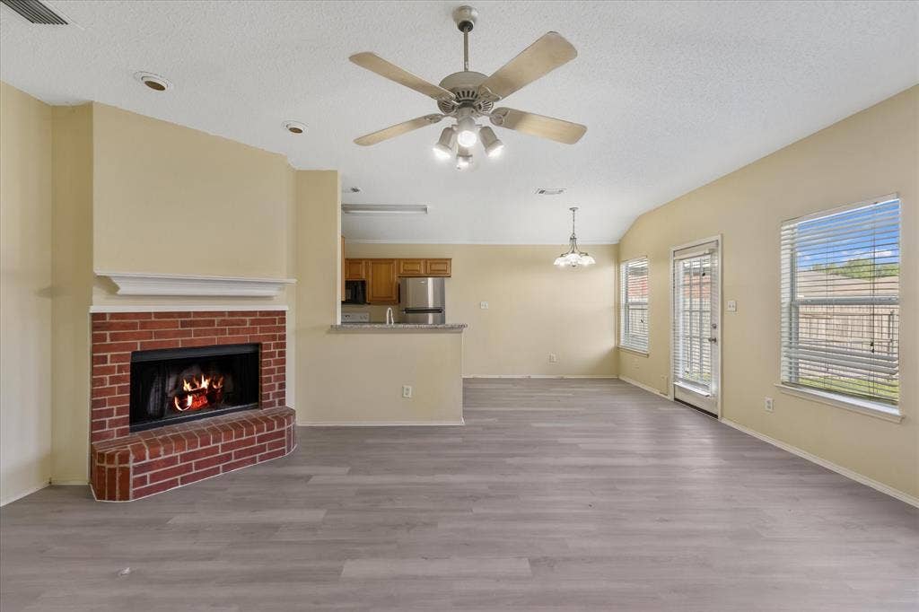 2312 Corral Drive, Fort Worth, TX 76133 Spacious living area featuring wood-finish flooring, brick-surround fireplace, ceiling fan, and multiple windows