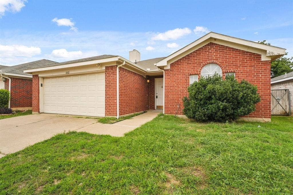 2312 Corral Drive, Fort Worth, TX 76133 Brick exterior featuring a two-car garage, concrete driveway, arched window detail, and front yard landscaping