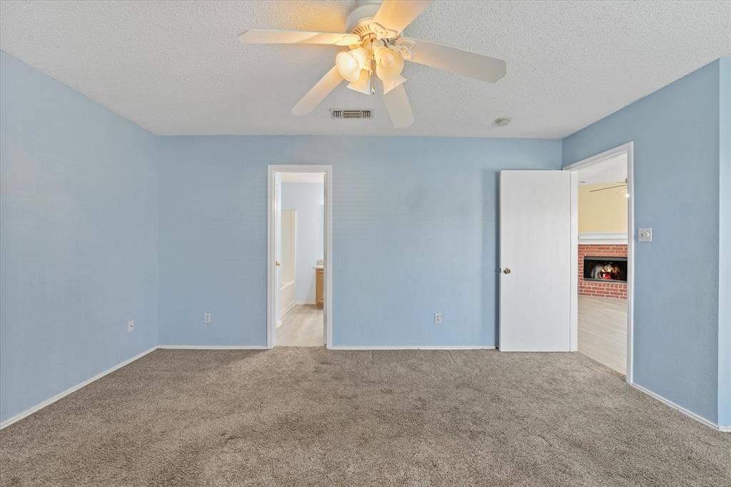 2312 Corral Drive, Fort Worth, TX 76133 Ceiling fan with light fixture, textured ceiling, carpet flooring, interior doors, and a visible fireplace surround