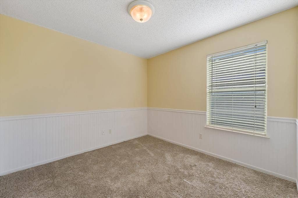 2312 Corral Drive, Fort Worth, TX 76133 Textured carpeting with a neutral finish, white wainscoting, and a window with blinds