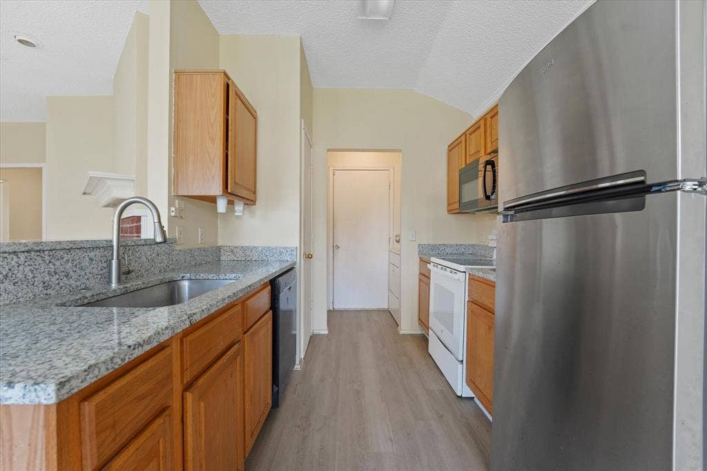 2312 Corral Drive, Fort Worth, TX 76133 Kitchen featuring wood cabinetry, light-toned countertops, a stainless steel refrigerator, and wood-finish flooring