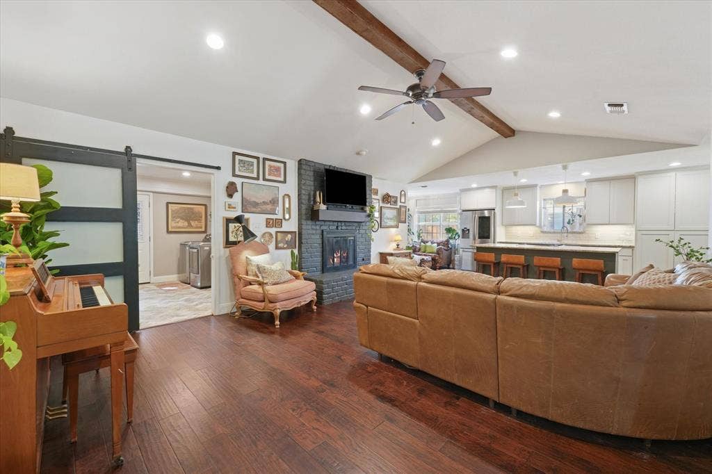 1112 Woodmount Court, Denton, TX 76209 Expansive open-concept living room with vaulted ceiling, exposed beam, hardwood floors, painted brick fireplace, and seamless flow into the renovated kitchen.