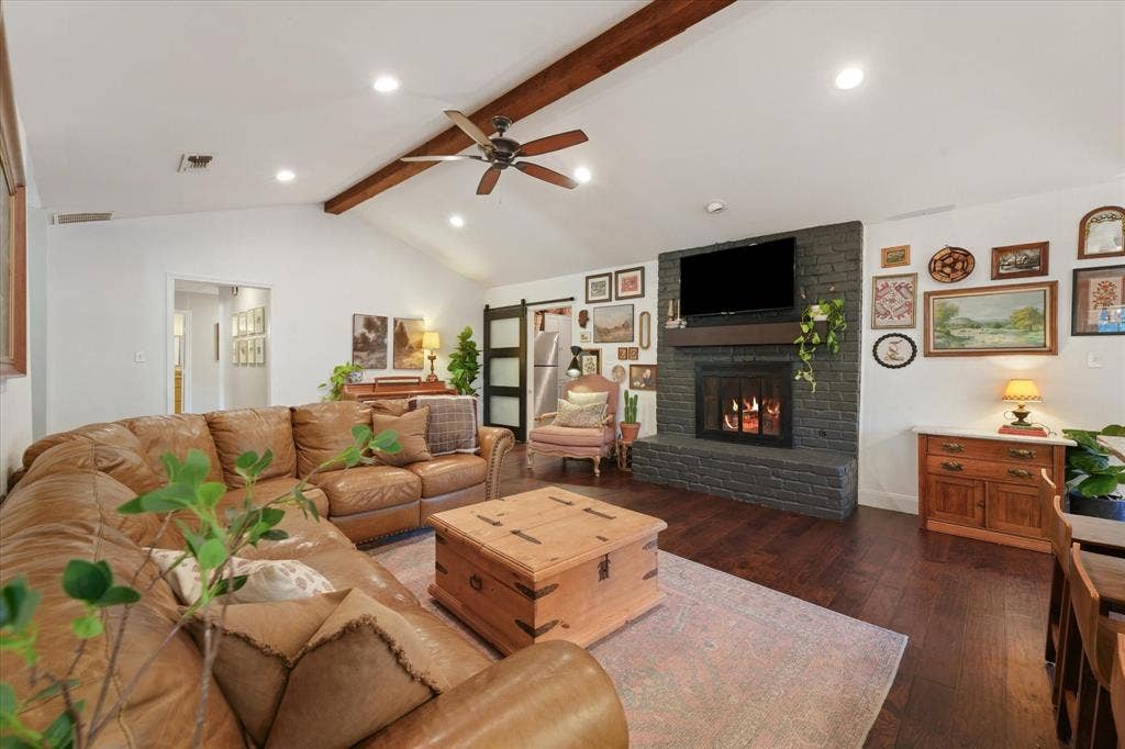 1112 Woodmount Court, Denton, TX 76209 Large family room featuring a painted brick fireplace, vaulted ceiling with exposed beam, hardwood flooring, and open sightlines to the kitchen and dining areas.
