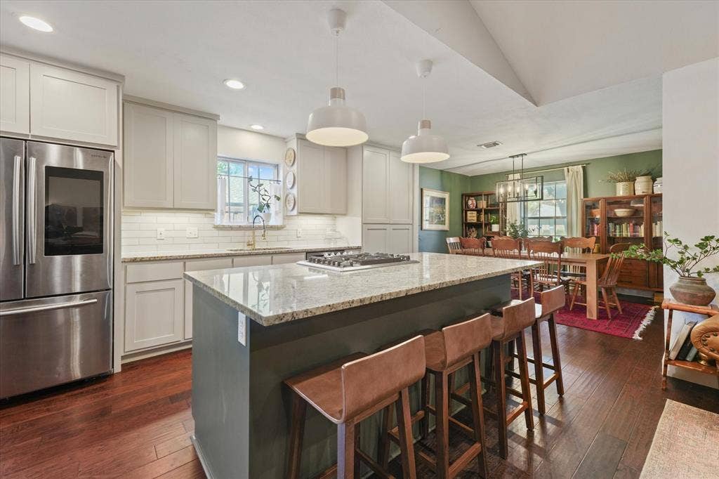 1112 Woodmount Court, Denton, TX 76209 Expansive kitchen with a large island offering seating for four, granite countertops, gas cooktop, updated lighting, and open access to the dining room.