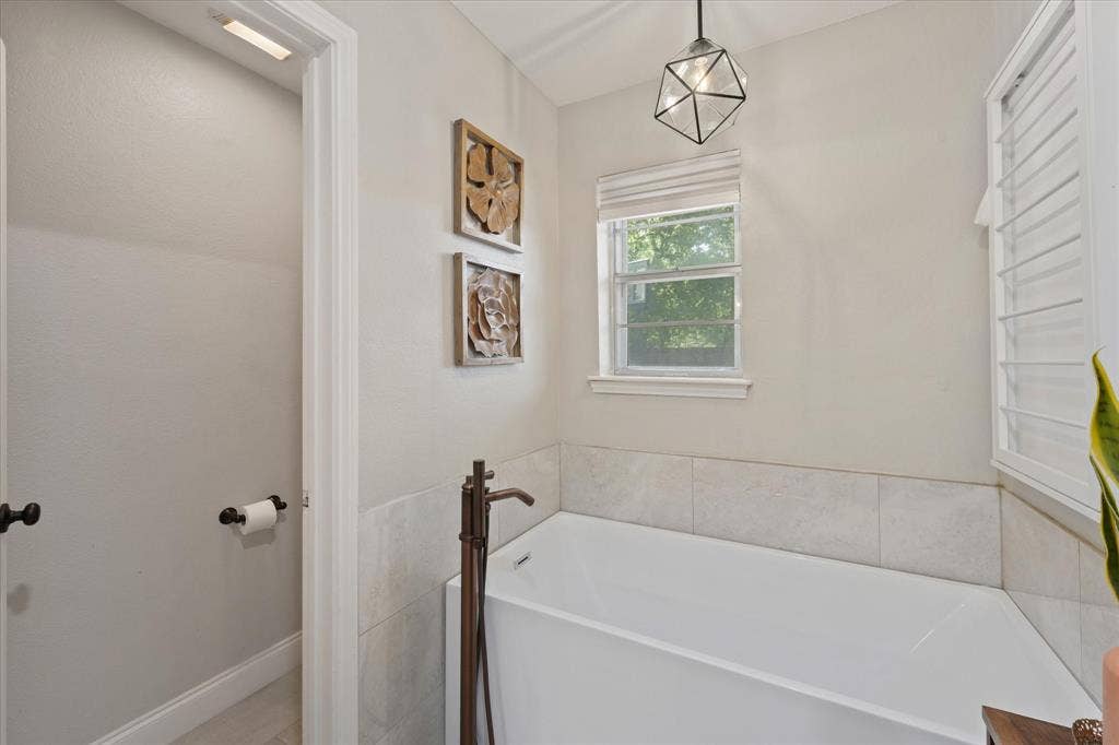 1112 Woodmount Court, Denton, TX 76209 Relaxing freestanding soaking tub with natural light, modern fixtures, and a peaceful retreat within the renovated primary bathroom.