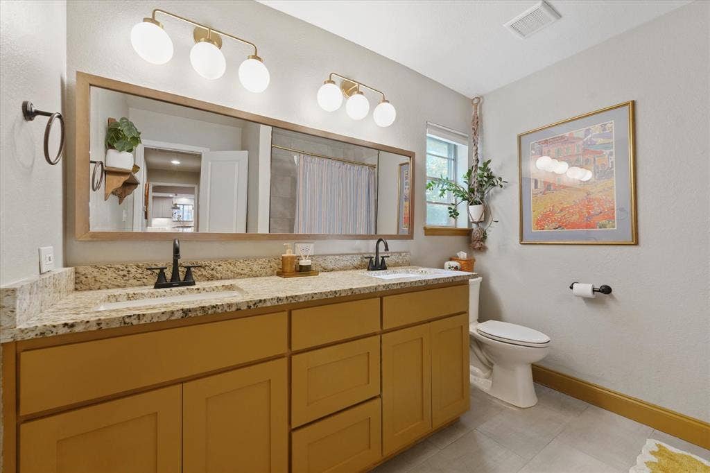 1112 Woodmount Court, Denton, TX 76209 Updated hall bathroom with dual granite vanities, modern lighting, updated fixtures, and abundant counter space serving the secondary bedrooms.