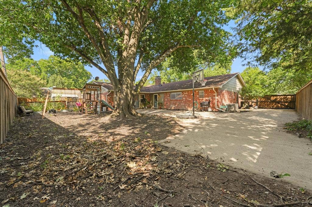 1112 Woodmount Court, Denton, TX 76209 Oversized backyard shaded by mature trees with an expansive concrete patio, plenty of room for entertaining, play, gardening, or future outdoor living, plus a storage building and privacy fence.