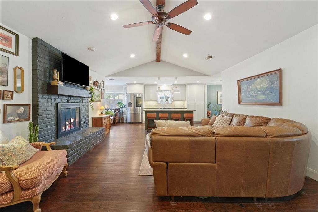 1112 Woodmount Court, Denton, TX 76209 Open living, dining, and kitchen layout with vaulted ceiling, exposed beam, painted brick fireplace, oversized island, and ideal space for everyday living and entertaining.