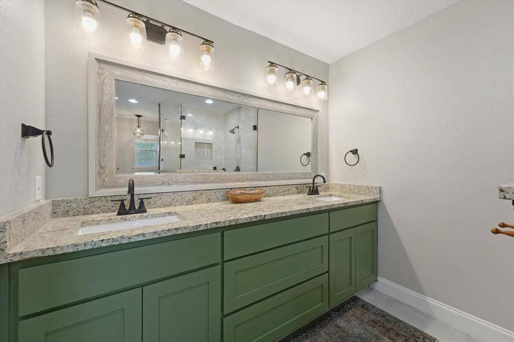 1112 Woodmount Court, Denton, TX 76209 Dual granite vanity with custom cabinetry, updated lighting, and generous storage in the beautifully remodeled primary bathroom.