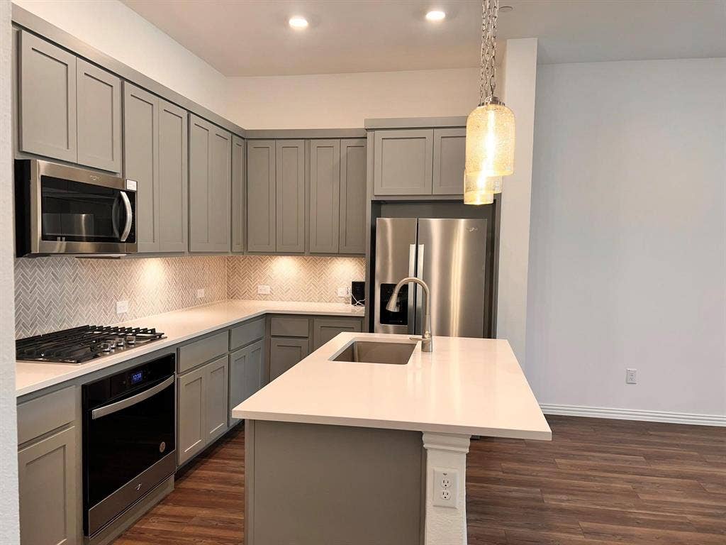 1054 Old Rosebud Drive, Allen, TX 75013 Modern kitchen featuring sleek grey cabinetry, stainless steel appliances, a herringbone tile backsplash, and an island with an undermount sink