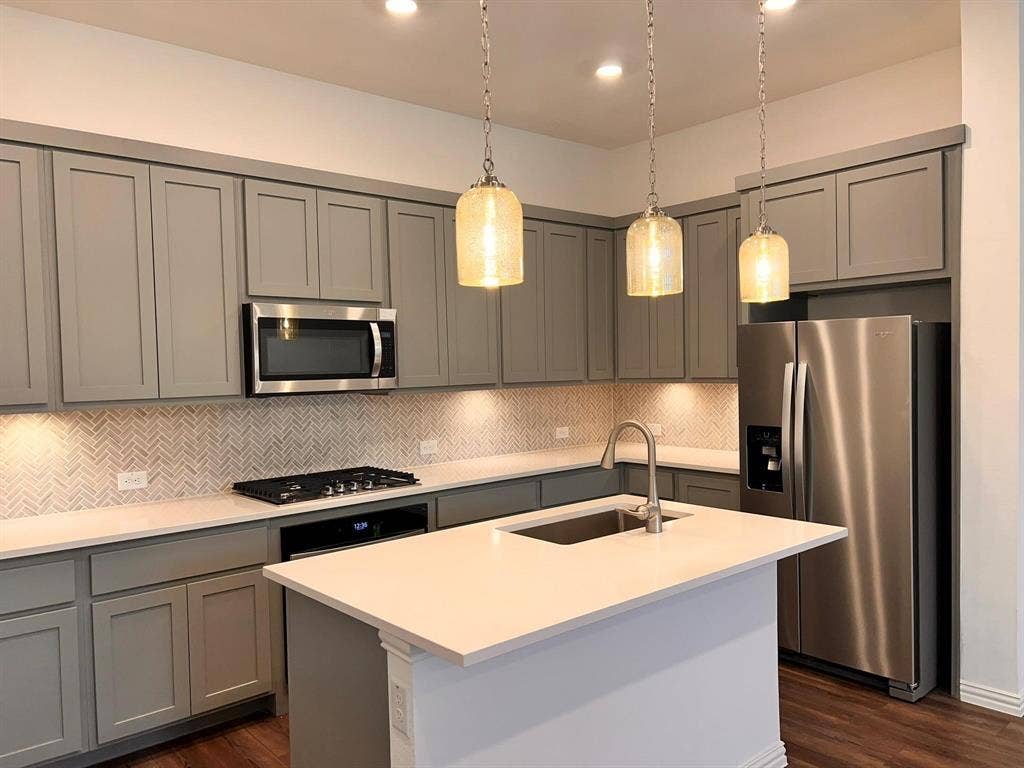 1054 Old Rosebud Drive, Allen, TX 75013 Kitchen featuring gray shaker cabinetry, stainless steel appliances, herringbone tile backsplash, an island with an integrated sink, and pendant lighting