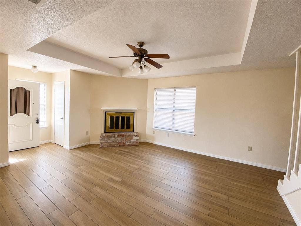 530 Rawls Circle, Irving, TX 75061 Spacious interior featuring wood-finish flooring, a tray ceiling with a ceiling fan, and a fireplace with a brick base
