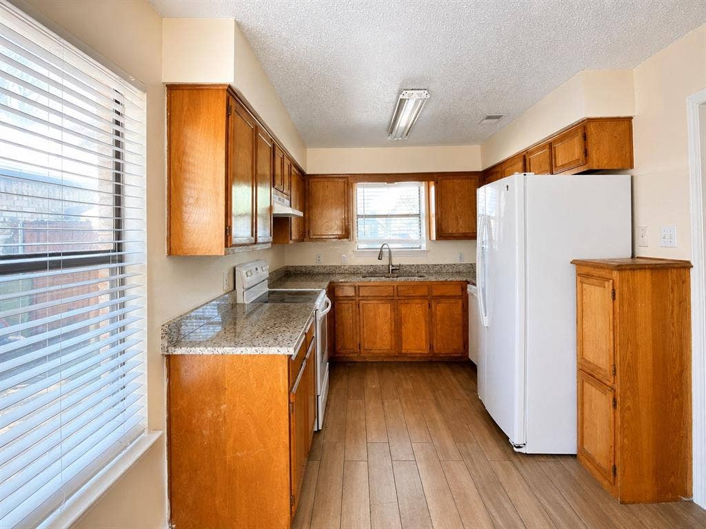 530 Rawls Circle, Irving, TX 75061 Kitchen featuring wood-finish flooring, wood cabinetry, granite countertops, and a stainless steel sink with a gooseneck faucet