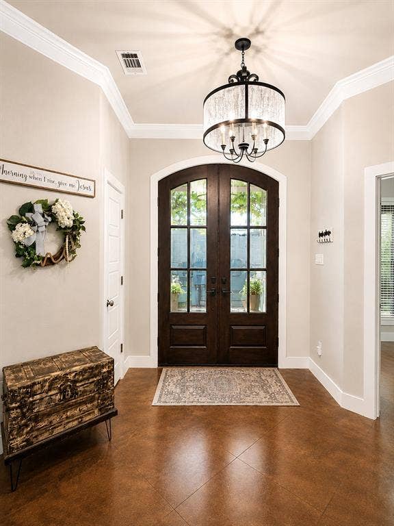 Entryway featuring rich brown flooring, a pair of arched dark wood doors with glass panels, and a decorative chandelier