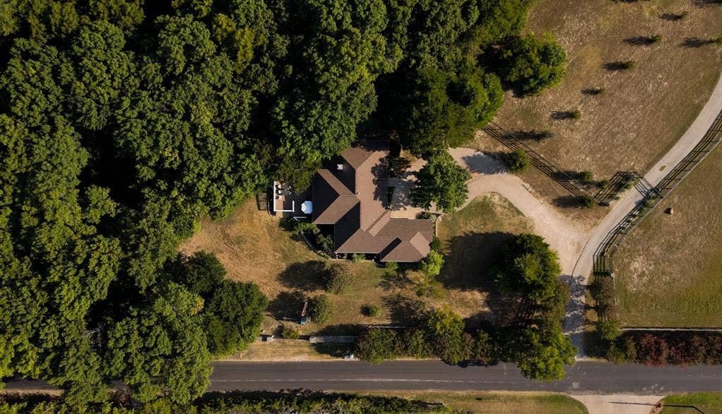 Expansive property featuring a brown-roofed residence nestled amongst mature trees, a private patio, and a dedicated driveway