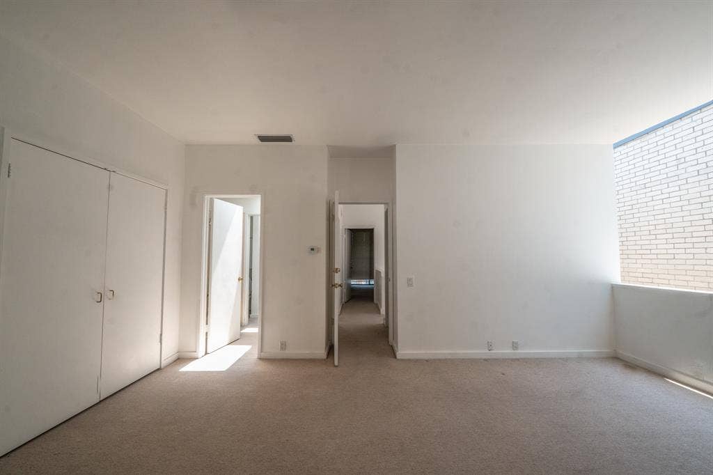 2818 Welborn Drive, #9, Dallas, TX 75219 Spacious room featuring neutral carpeting, white walls, two bi-fold closet doors, and doorways to bathroom