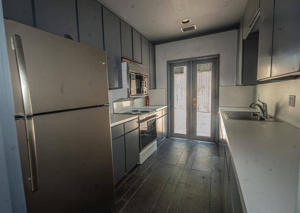 2818 Welborn Drive, #9, Dallas, TX 75219 Galley kitchen featuring dark cabinetry, white countertops, and stainless steel appliances including a refrigerator and microwave