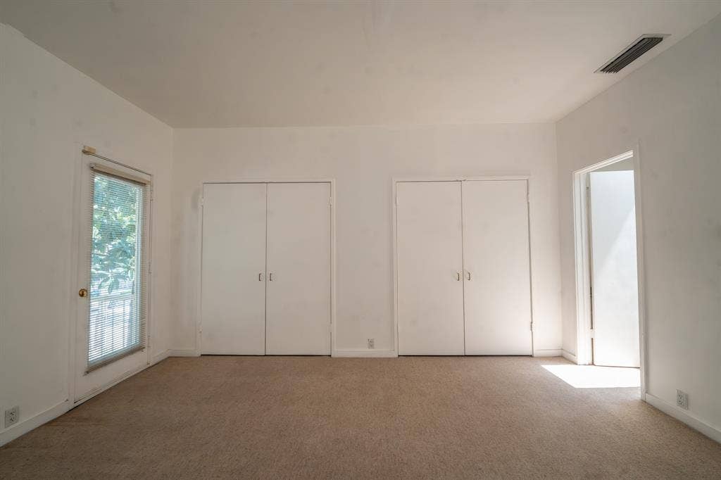 2818 Welborn Drive, #9, Dallas, TX 75219 Carpeted room featuring a ceiling vent, two sets of bi-fold closet doors, a white baseboard trim, and a glass-paneled exterior door
