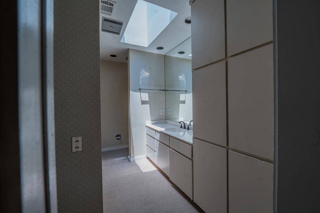 2818 Welborn Drive, #9, Dallas, TX 75219 Skylight-illuminated vanity space featuring an integrated sink, polished countertop, dark-finish faucet, and extensive built-in cabinetry