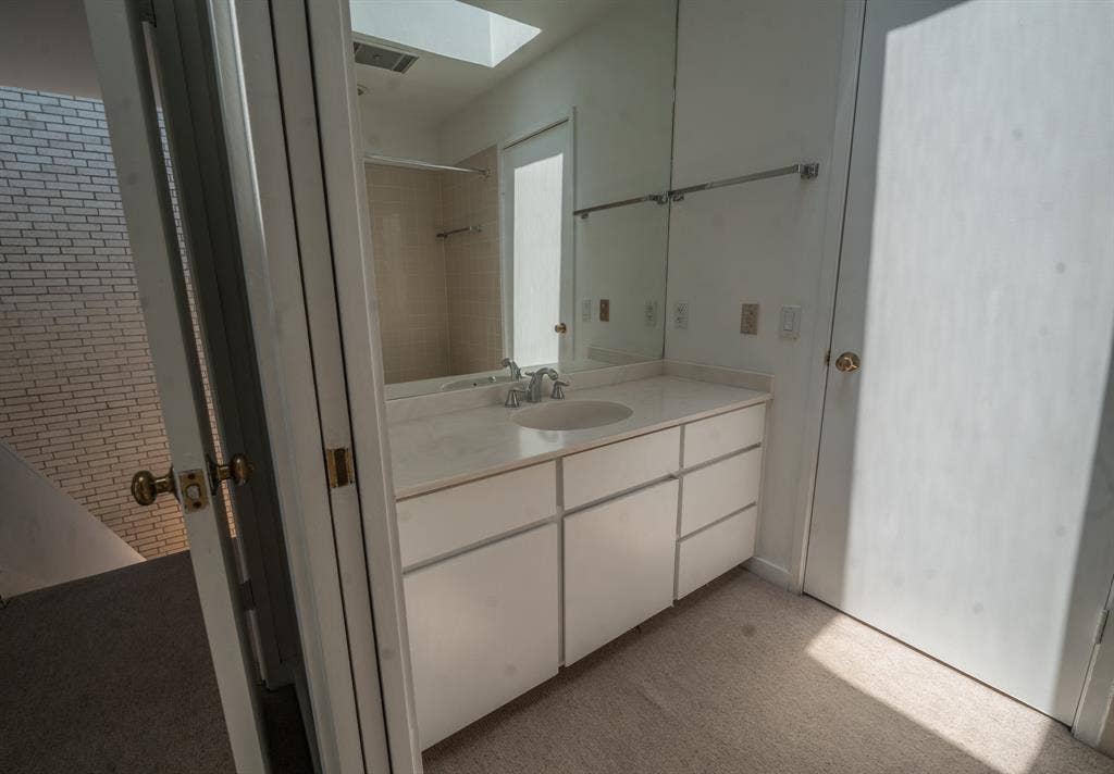 2818 Welborn Drive, #9, Dallas, TX 75219 White vanity with an integrated sink and countertop, mirrored wall, recessed lighting, and a skylight