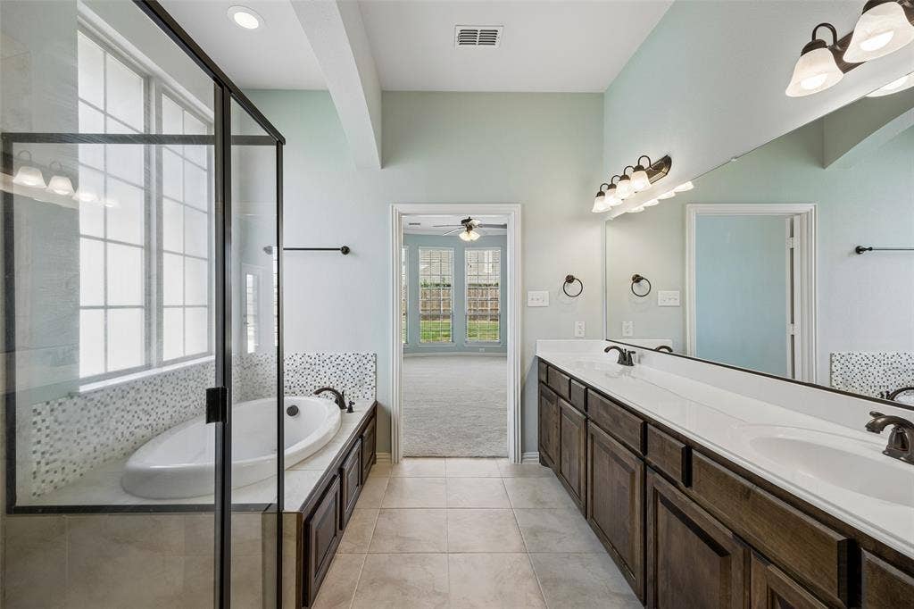 Bathroom featuring a built-in soaking tub with mosaic tile surround, a spacious double vanity with integrated sinks, and an enclosed shower with clear glass panels