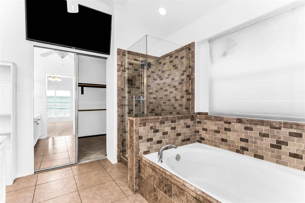11404 Amber Valley Drive, Frisco, TX 75035 Spa-inspired primary bathroom featuring a soaking tub with tile surround, walk-in shower with glass enclosure and mosaic tile walls in warm earth tones, tile flooring, and dual vanity with ample storage