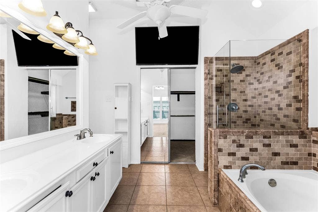 11404 Amber Valley Drive, Frisco, TX 75035 Dual vanity with white cabinetry, tile flooring, glass-enclosed shower with tile surround, and a built-in soaking tub with tile surround