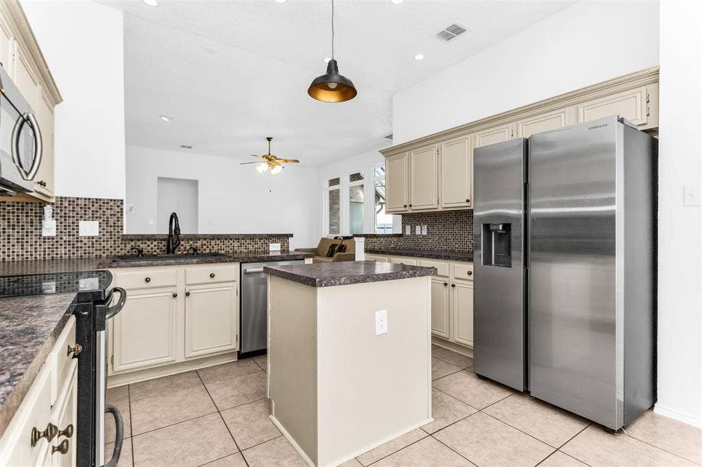 11404 Amber Valley Drive, Frisco, TX 75035 Cream-painted cabinetry with dark hardware, a mosaic tile backsplash, and a black countertop