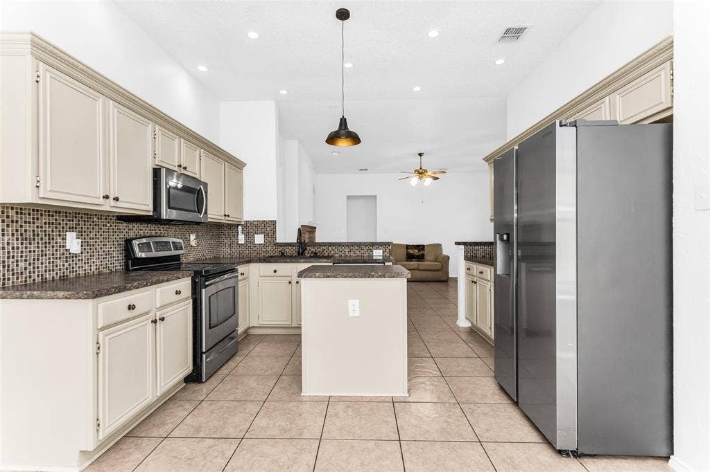 11404 Amber Valley Drive, Frisco, TX 75035 Spacious kitchen featuring cream-colored cabinetry, stainless steel appliances, granite countertops, a large center island with seating, mosaic tile backsplash, tile flooring, and recessed ceiling lighting