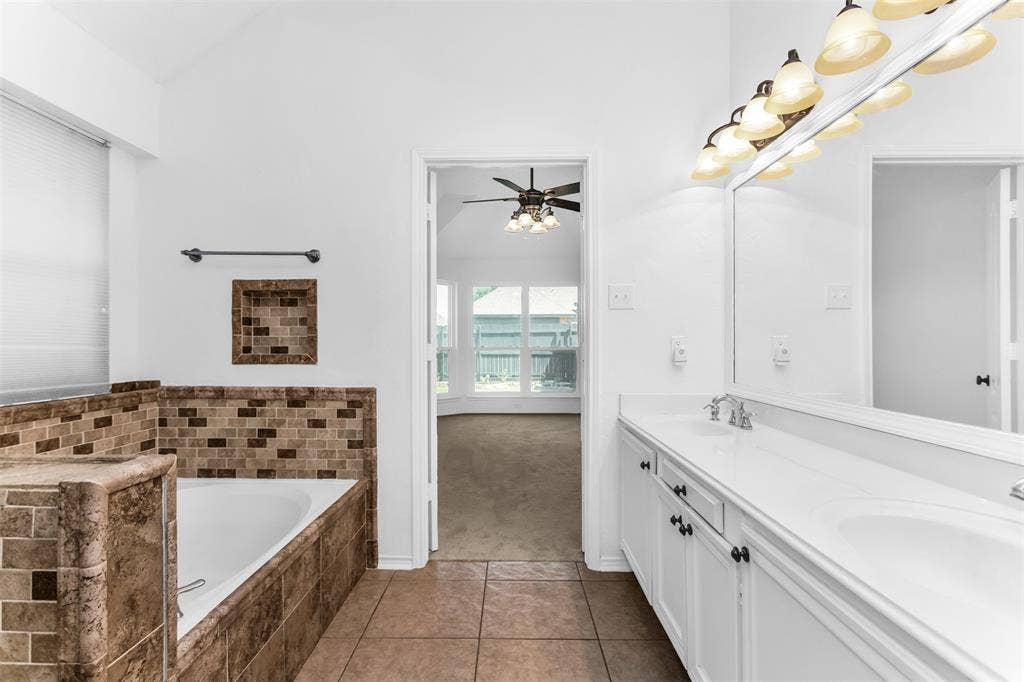 11404 Amber Valley Drive, Frisco, TX 75035 Tile flooring, built-in bathtub with tiled surround, dual vanity with white cabinets, and an expansive wall-mounted mirror with overhead lighting