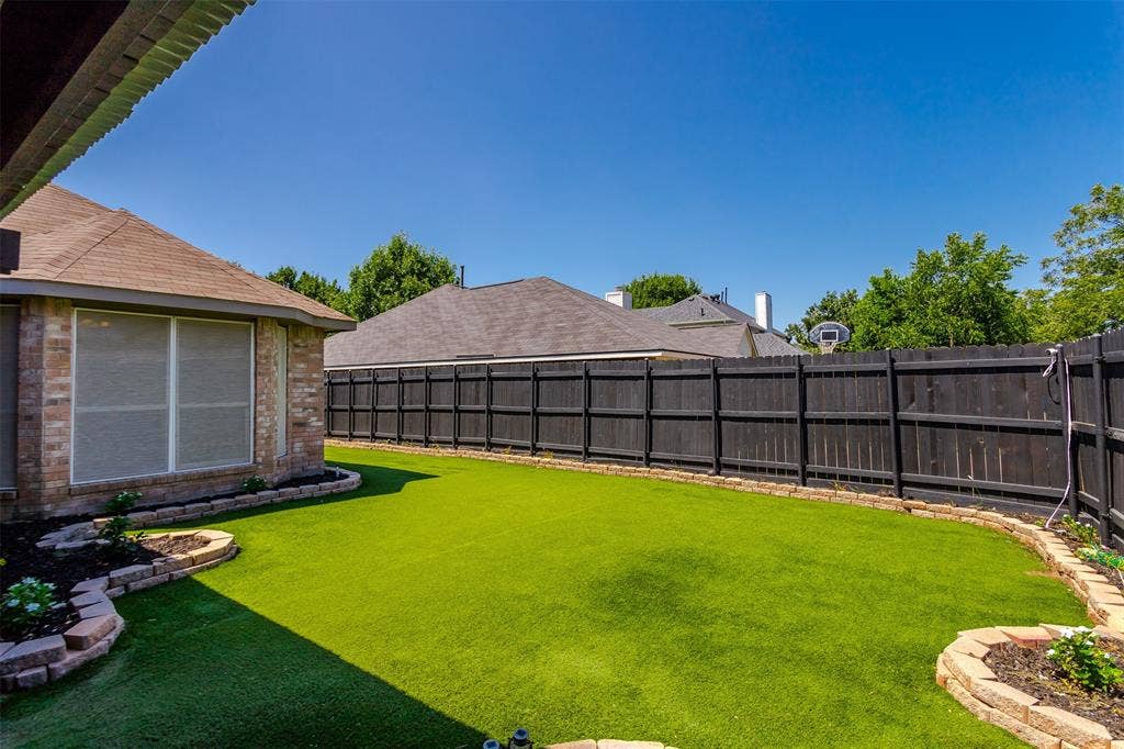 11404 Amber Valley Drive, Frisco, TX 75035 Expansive backyard featuring a lush, manicured lawn bordered by mature landscaping and flowering beds