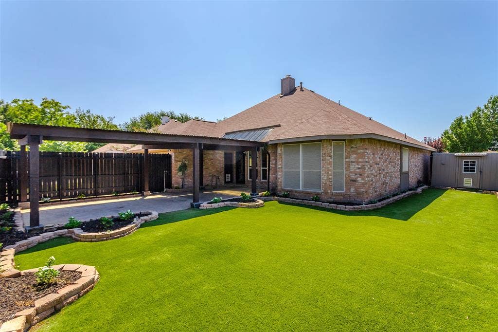 11404 Amber Valley Drive, Frisco, TX 75035 Brick exterior with a covered patio, extensive artificial turf, and a storage shed
