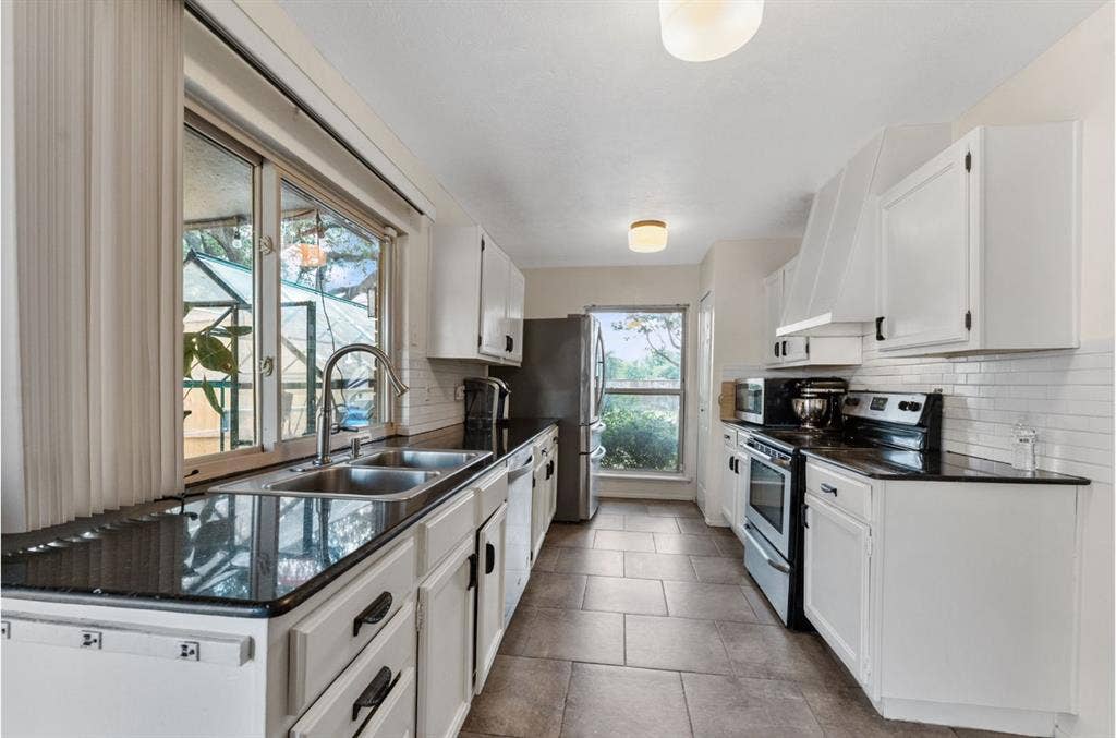 Kitchen featuring white cabinetry, black countertops, tile flooring, and a stainless steel double basin sink
