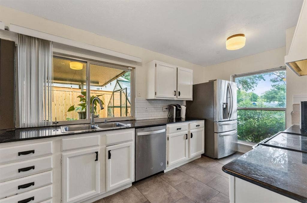 Kitchen featuring white cabinetry, dark stone countertops, stainless steel appliances, tile flooring, and a subway tile backsplash