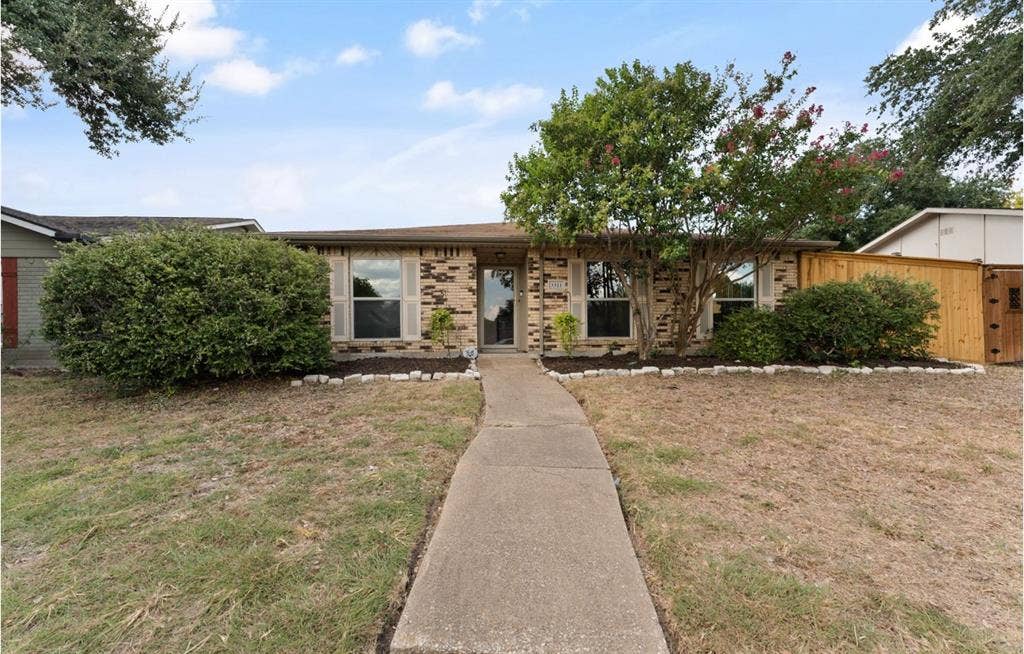 Brick exterior with a concrete walkway, established landscaping, and a wood privacy fence