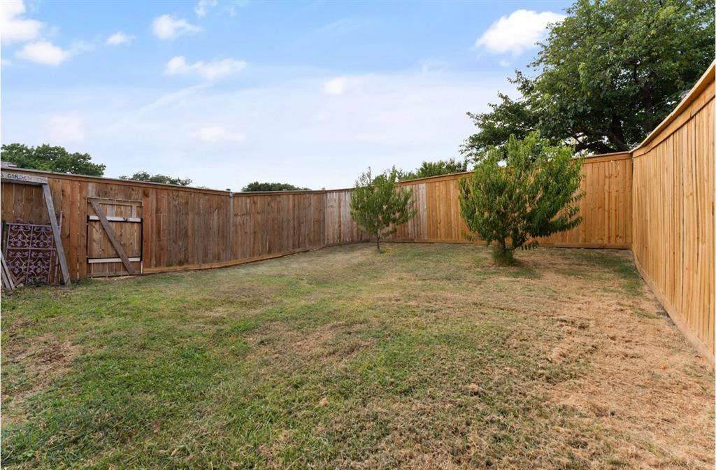 Fenced backyard with a wooden gate and mature trees