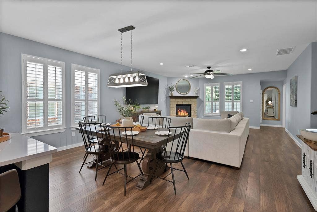 Open-concept living space featuring wood-finish flooring, a stone-faced fireplace with a mantel, and recessed lighting