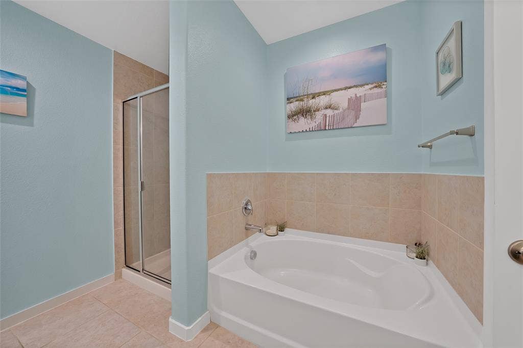 Corner garden tub with tile surround, glass-enclosed shower, light blue painted walls, and tile flooring